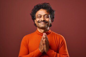 Obraz premium Portrait of a satisfied indian man in his 40s joining palms in a gesture of gratitude in solid color backdrop