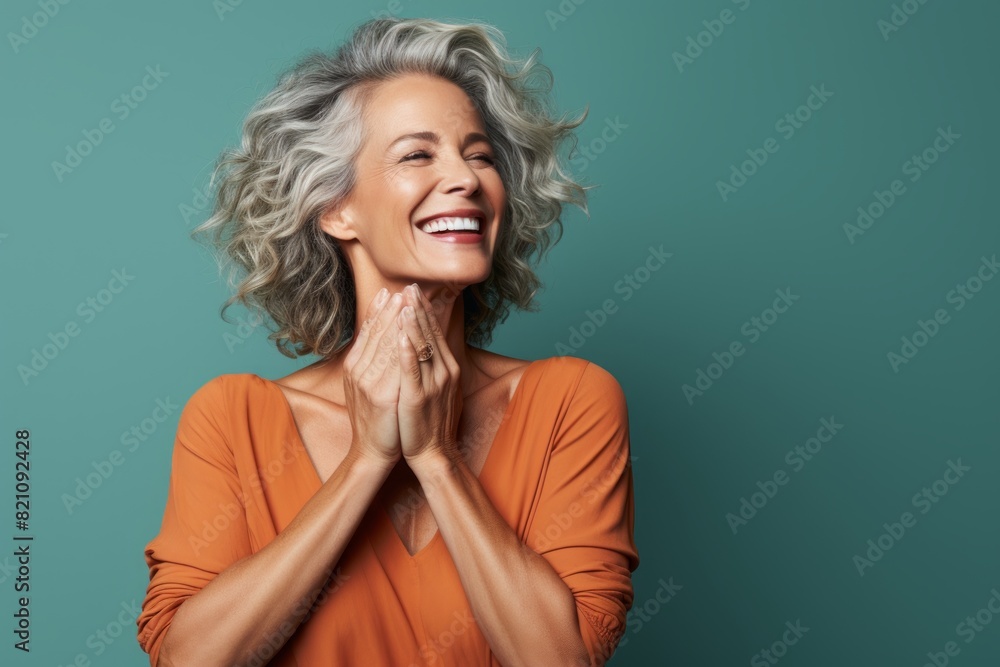 Wall mural portrait of a joyful woman in her 50s joining palms in a gesture of gratitude over solid color backd - Wall murals