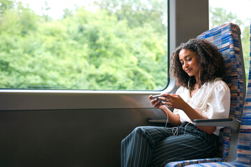 Businesswoman Commuting To Work On Train Streaming Movie Or Show To Mobile Phone Wearing Earphones © Monkey Business