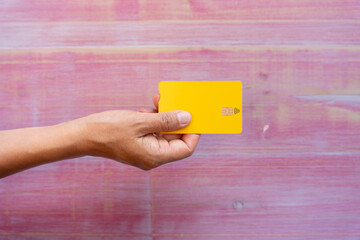 Woman hand holding yellow credit card on pink wooden background stripping. Contact less use concept
