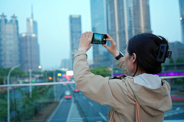 Woman Capturing Cityscape on Smartphone at Dusk