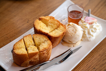 White plate holds delectable serving of honey toast, complemented by vanilla ice cream, whipped cream and drizzle of honey