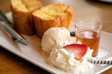 Delectable serving of honey toast comes with scoop of vanilla ice cream, whipped cream topped with strawberry, and side of honey