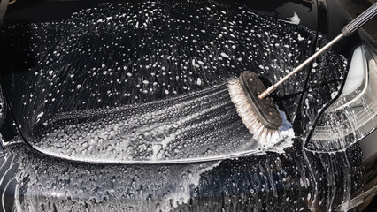 Cropped image of wheel of luxury black car in outdoors self-service car wash, covered with cleaning...