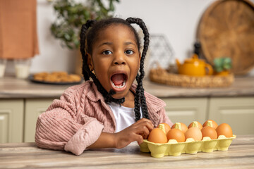 Black little girl with excited facial expression sitting in kitchen with eggs on counter top