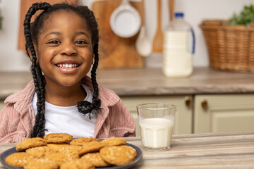 Cheerful multicultural little girl enjoying cookies and milk during breakfast
