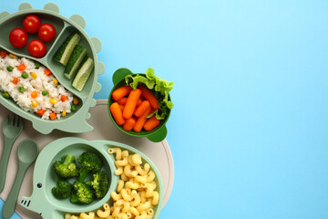 Kids nutrition concept. Fresh foods in green silicone dishes against a blue background. It includes tomatoes, cucumbers, mixed vegetable rice, baby carrots, broccoli, and pasta.