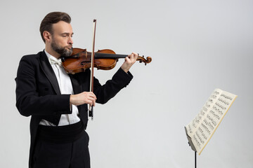 Bearded male violinist playing violin in front of sheet music