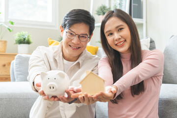 Happy asian family young couple love hand holding piggy bank to save and model house for saving...