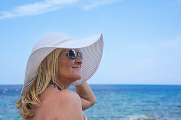 A mature woman in a hat and sunglasses on the beach on vacation.