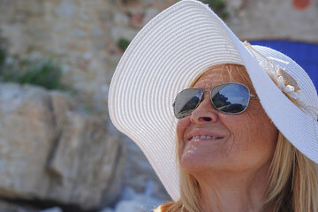 portrait of a mature tourist in a white hat and sunglasses smiling on summer vacation