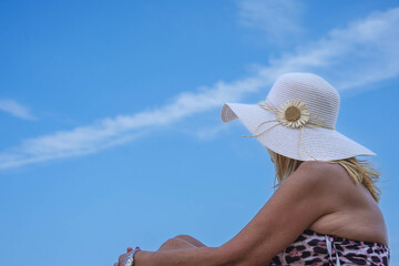 A mature woman in bikini sitting on beach on summer vacation with blue sky