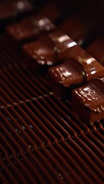Bars of sweets covered with chocolate. Chocolate bars move along conveyor belt at confectionery factory for the production of sweets. Close up. Vertical video