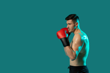 A man wearing boxing gloves strikes a dynamic pose on a vibrant green background. His stance exudes strength and determination as he showcases his boxing skills, copy space