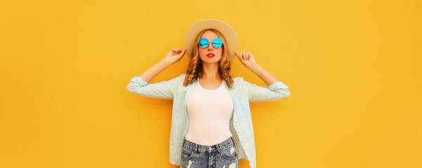 Summer portrait of stylish blonde young woman posing wearing straw hat on bright yellow background