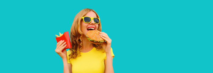 Portrait of happy cheerful young woman eating burger fast food and french fries