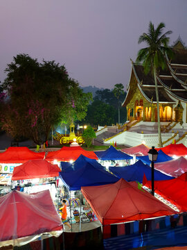 Colorful night market in luang prabang stalls with a variety of goods, illuminated temple in the background, creating a vibrant evening scene