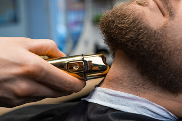 Master barber employs an automatic trimmer to groom the clients beard at the barbershop.