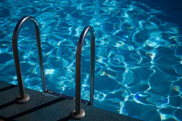 A metal ladder is in the water. The water is clear and calm. The ladder is in the middle of the pool.