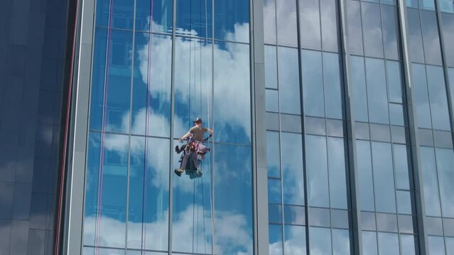 Aerial shot - worker suspended on a red rope cleaning windows on a high rise building.