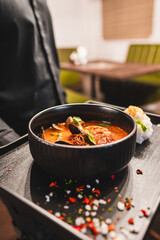 A vibrant bowl of soup with assorted ingredients, garnished with fresh herbs, presented on a tray