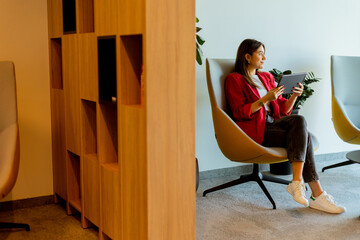 Young professional woman working on tablet in modern office seating area in morning light