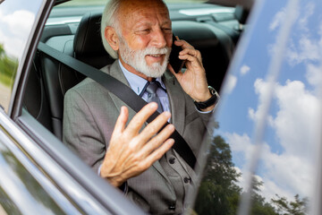 Elegant senior businessman chatting on phone while riding in a luxury car