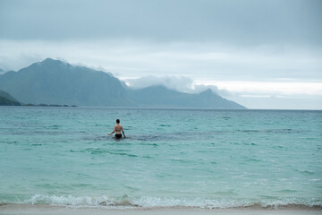  Junge Frau schwimmt im türkisblauen Nordpolarmeer umgeben von Bergen auf den Lofoten während es...