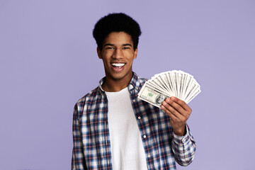 Finance and money saving. Excited guy holding lots of dollars, pink studio background