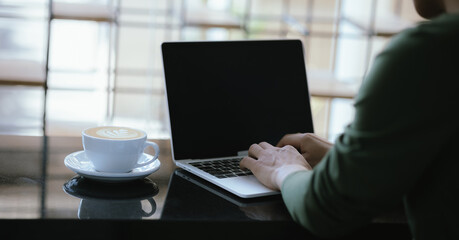 Cropped view of man at coffee shop Working on laptop computer with coffee cup on table in cafe