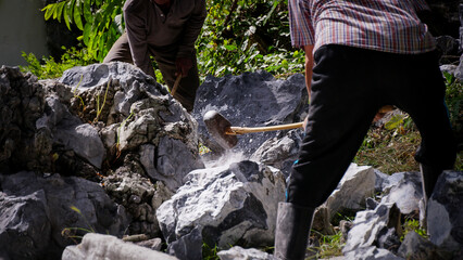 Two worker breaking big rocks or stones with a hammer to build foundation, boundary wall in a construction site.