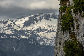 The view depicts a mountain towering over a valley, with lush greenery contrasting the rugged...