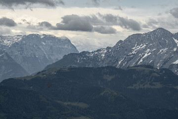The view depicts a mountain towering over a valley, with lush greenery contrasting the rugged...