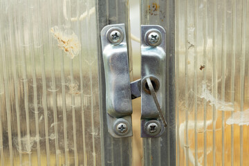 Metal latch on the doors to a polycarbonate greenhouse