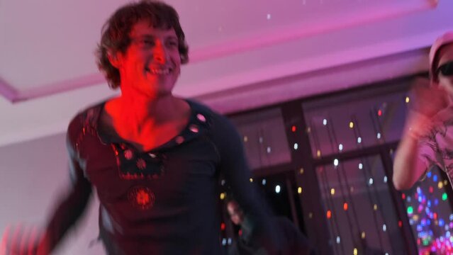 Dynamic movements of friends getting down dance to beats at home party bash with neon lights vibe, young men jump and dances celebrating birthday, weekend holiday background.