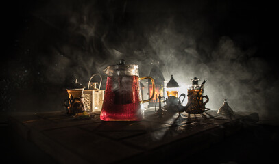 Arabian tea in glass with eastern snacks on a carpet on dark background with lights and smoke....