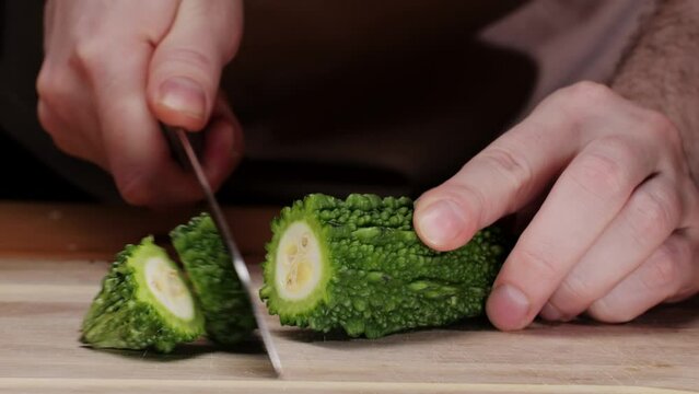 Cutting a bitter gourd on wooden desk by knife close-up, a vegetable often used as an ingredient in cuisine, is placed on a wooden table. This terrestrial plant is