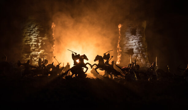 Medieval battle scene with cavalry and infantry. Silhouettes of figures as separate objects, fight between warriors on dark toned foggy background. Night scene.