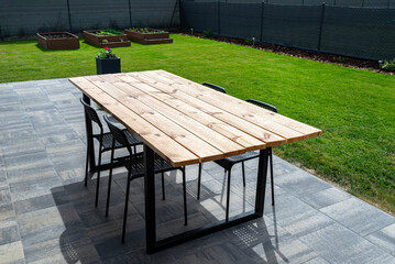 A modern table made of raw wood covered with yacht varnish, standing on the garden terrace.