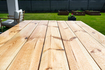 A modern table made of raw wood covered with yacht varnish, standing on the garden terrace.