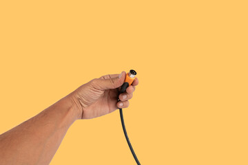 Black male hand holding a MIDI audio cable isolated on yellow background