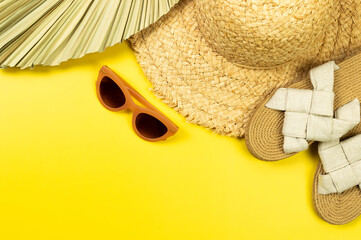 Top view of straw hat, dried palm leaf, slippers and sunglass on yellow background. Summer fashion,...