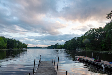 Naklejka premium Looking out onto a Wisconsin lake from a boat dock while the last rays of sunlight play in the clouds and are reflected in it's calm surface.