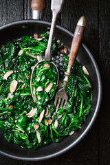 Tasty stewed spinach in frying pan with garlic and nuts close up. Healthy vegetarian food. top view