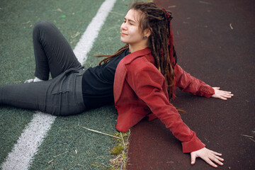 A happy teen girl lies on the grass on the playground. Daytime, stadium, open air