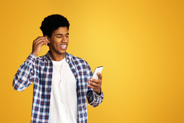 Happy african-american guy listening music with headphones and mobile phone, orange background