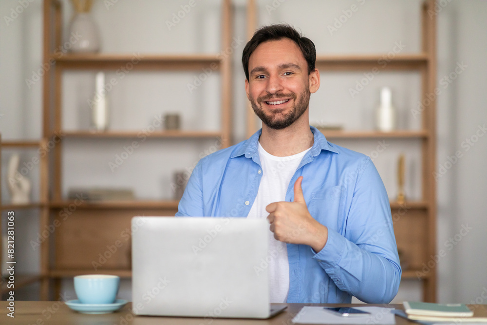Poster a man is seated at a table, using a laptop. he is smiling and giving a thumbs up gesture, indicating