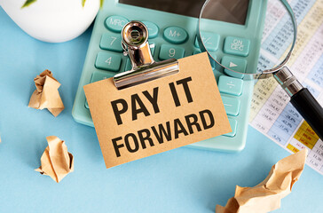 PAY IT FORWARD text on a notebook with pen on wooden background