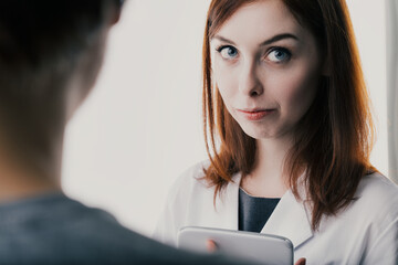 Auburn-haired woman, lab coat, tablet, serious expression