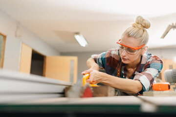 Attractive middle aged woman carpenter designer works with ruler, make notches on the tree in workshop. Image of modern femininity. Concept of professionally motivated women